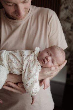 A series of photos showing a sleeping newborn baby swaddled in a white floral print blanket.
