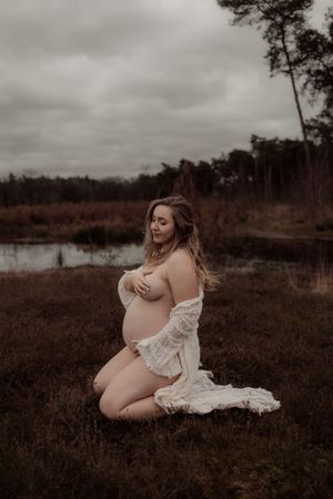 Artistic maternity photos in a rustic field setting with moody overcast skies and natural surroundings.