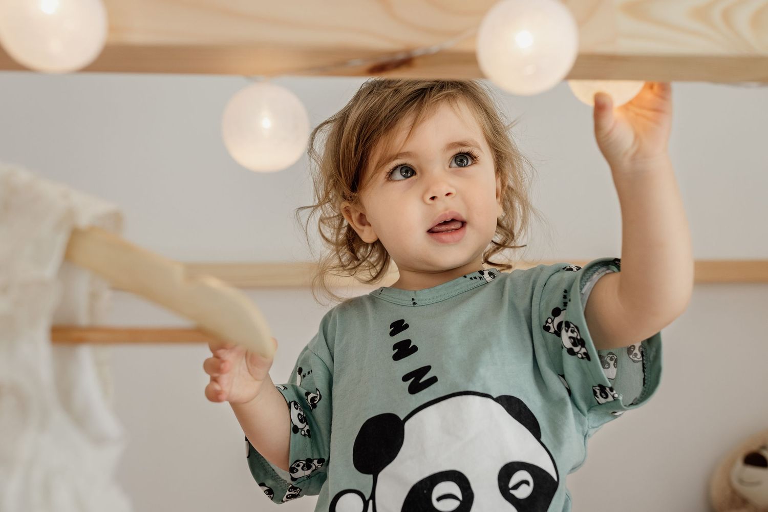 Baby in mint green dinosaur print dress plays with lantern decorations in a bright room.