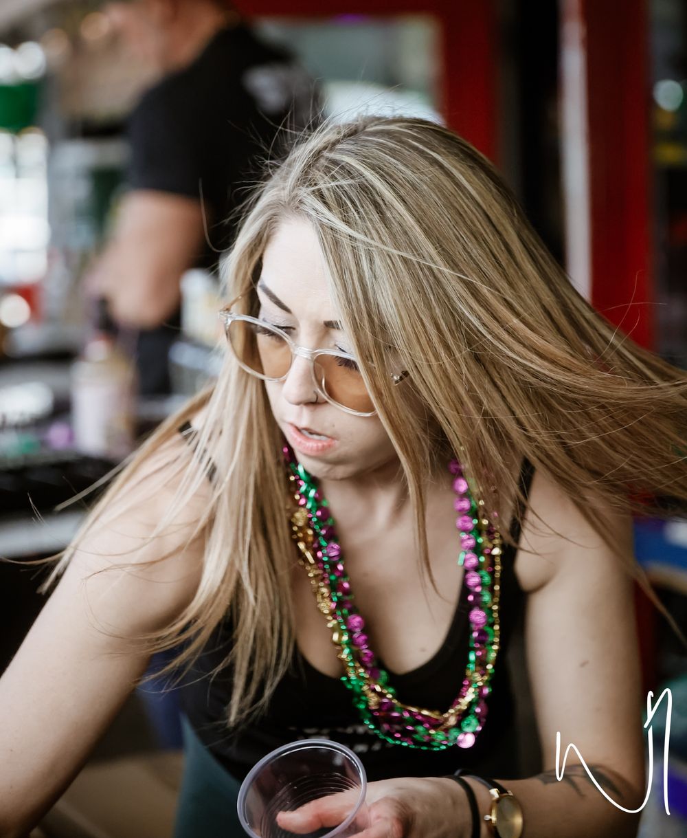 A person wearing colorful Mardi Gras beads takes a drink at a celebration.