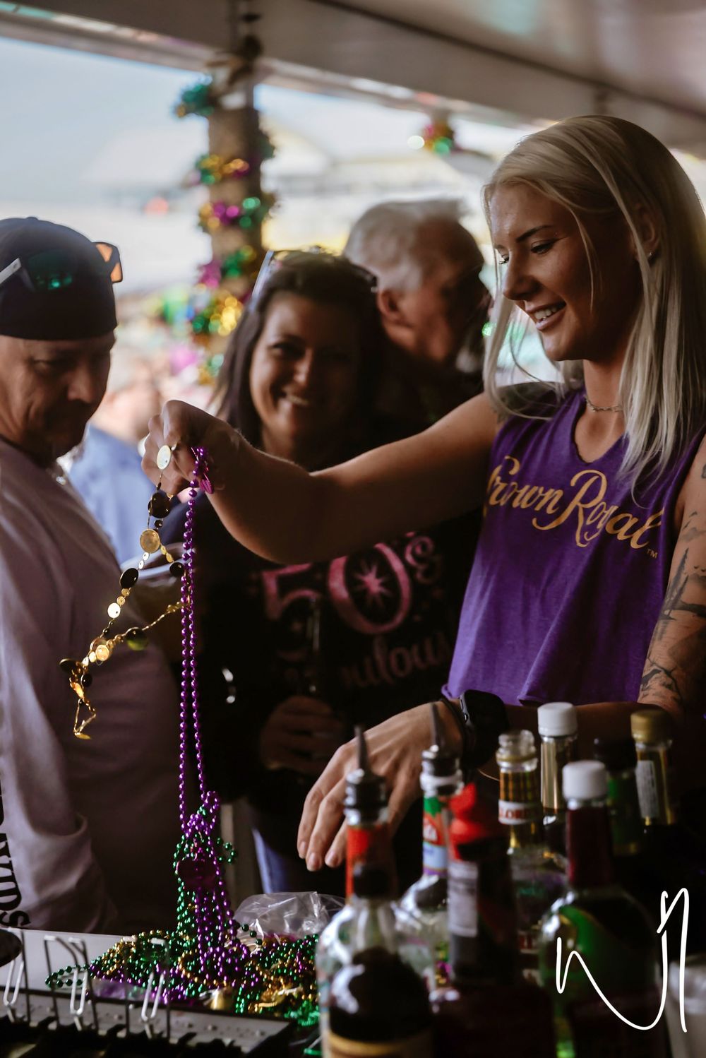 A sequence of people pouring and mixing drinks at a bar with purple beaded necklaces visible in the scene.