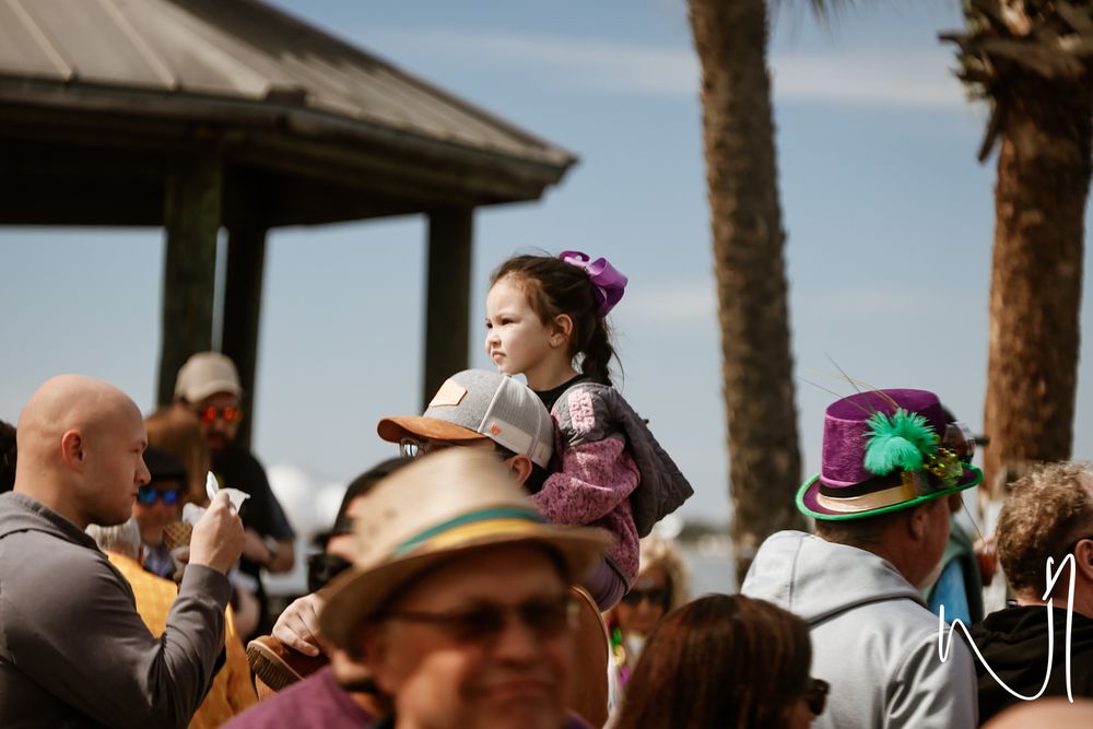 A crowd gathers outdoors under palm trees during a festive daytime celebration.