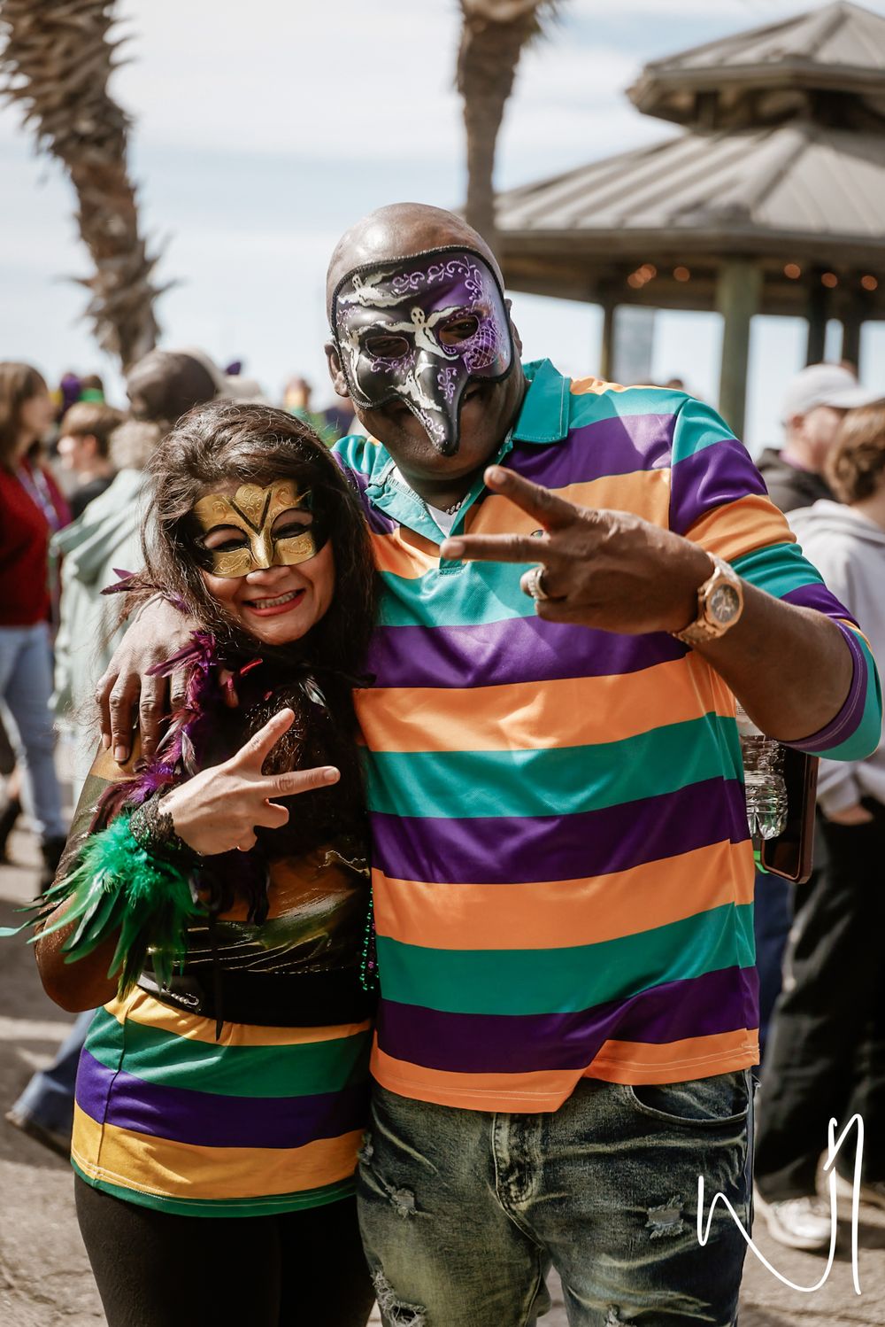 Friends in carnival masks and striped clothing embrace and pose together at an outdoor event.