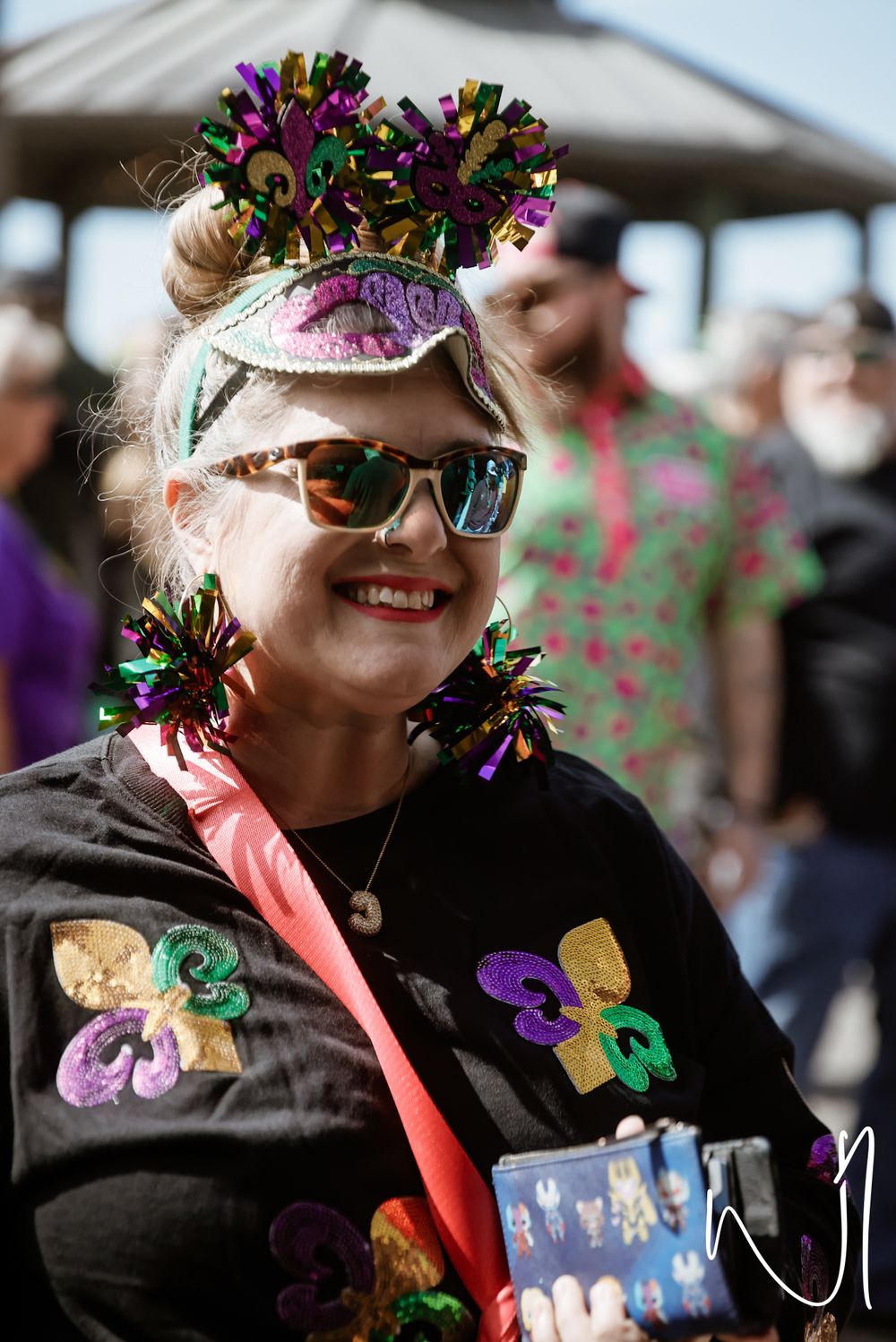 A person in festive Mardi Gras attire and decorative crown smiles during a celebration.