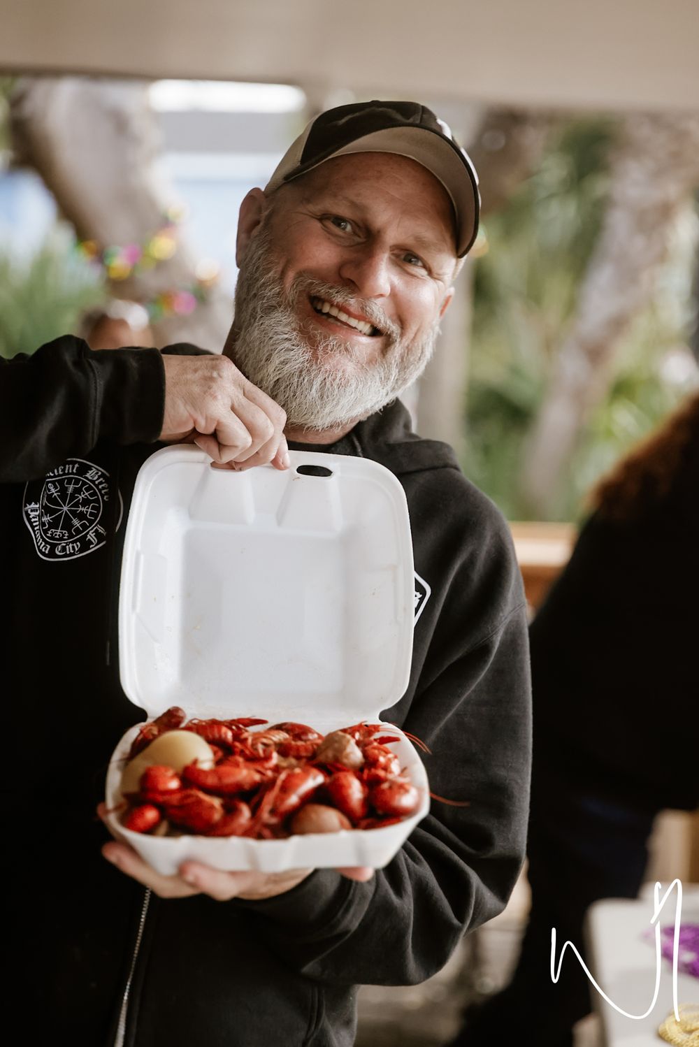 A person in a black hoodie displays a container of fresh crawfish.