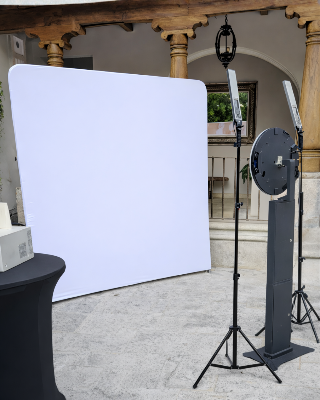 A photography lighting setup with a white reflector panel and black stands in an outdoor covered area.