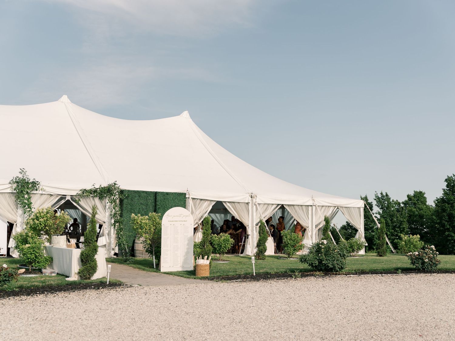 White wedding tents set up in a grassy outdoor venue with trees in the background on a cloudy summer day.