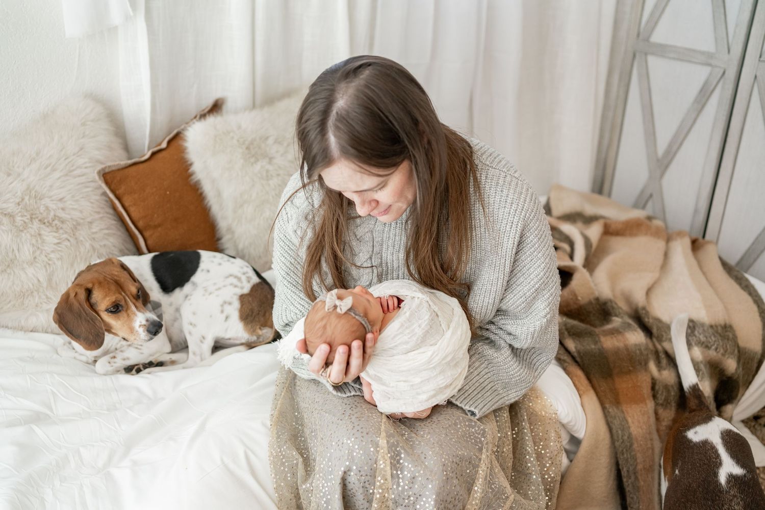 Beagle puppy lies on white bed sheets while person pets its head in cozy home setting.