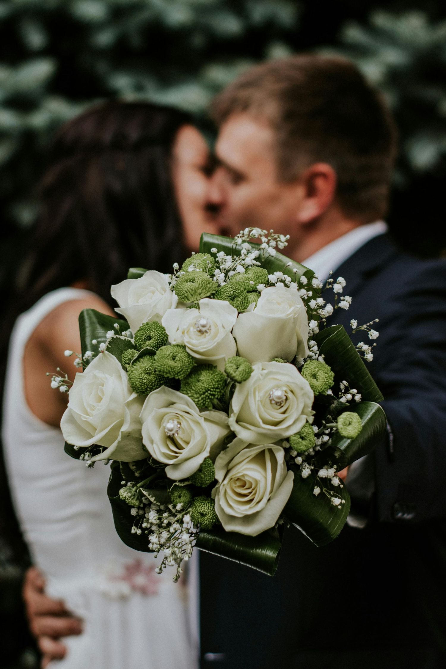 Classic white rose wedding bouquet with baby's breath held between couple.