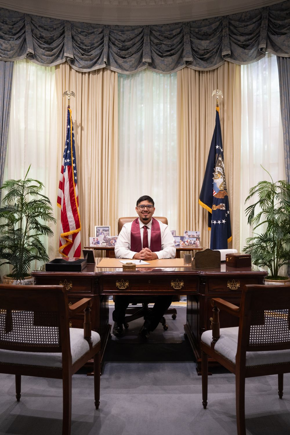 Texas A&M graduate posing at the replica Resolute Desk in the Oval Office exhibit at the George H.W. Bush Presidential Library in College St