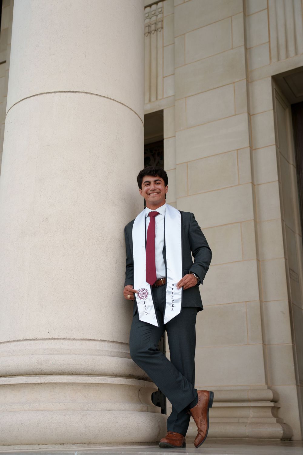 A well-dressed young man in a suit and tie stands confidently in front of a stone building.