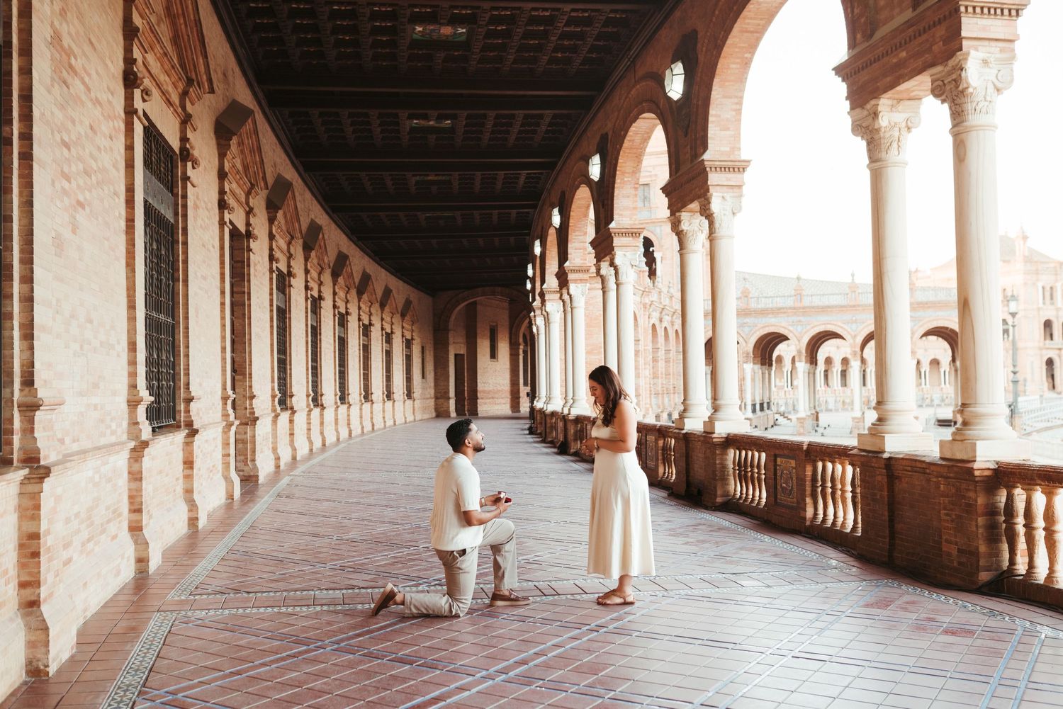 Couple explores Plaza de España in Seville, with woman in red dress against ornate architecture.