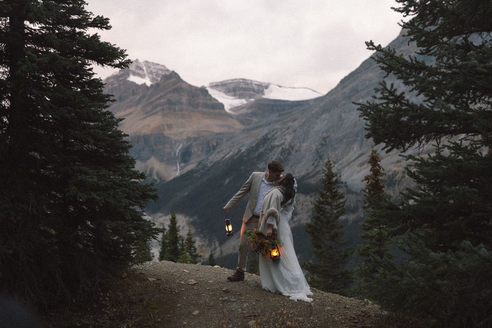 bride and groom kiss at dawn holding old fashioned lanterns