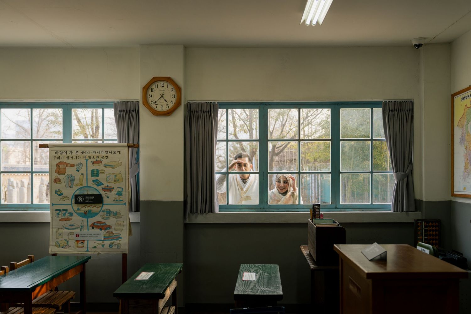 An empty classroom with windows showing bare winter trees outside and a clock on the wall.