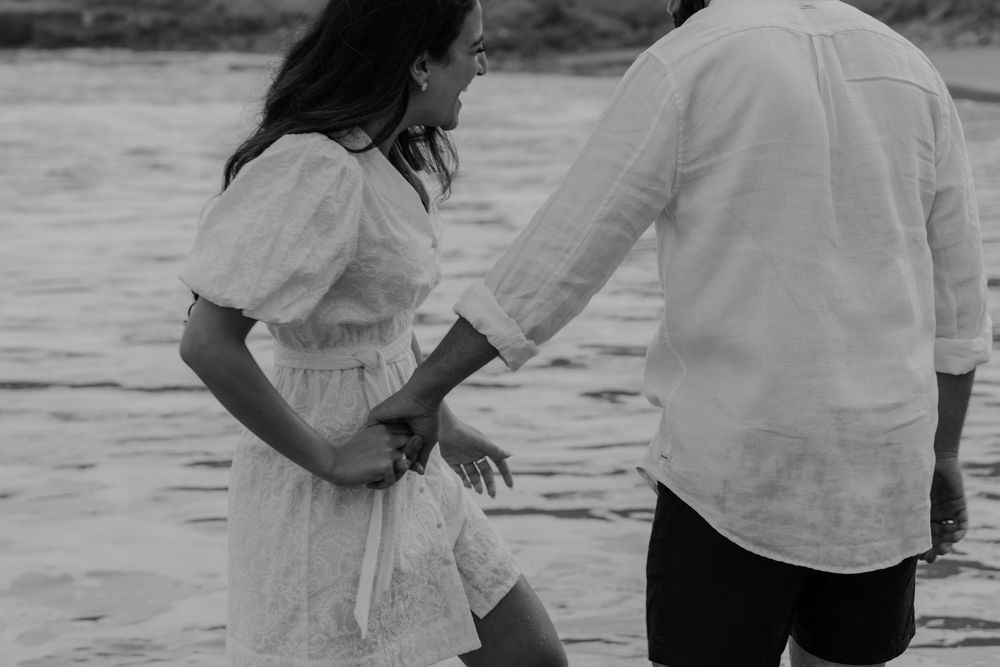 Black and white photo of couple holding hands near ocean waves on beach.