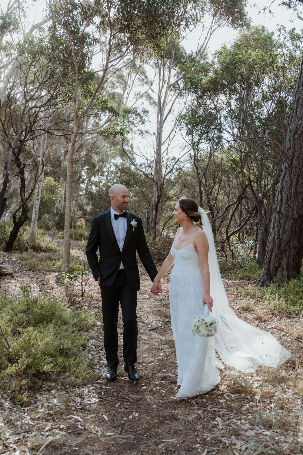 Bride and groom walk hand in hand through a native Australian bushland trail on their wedding day.