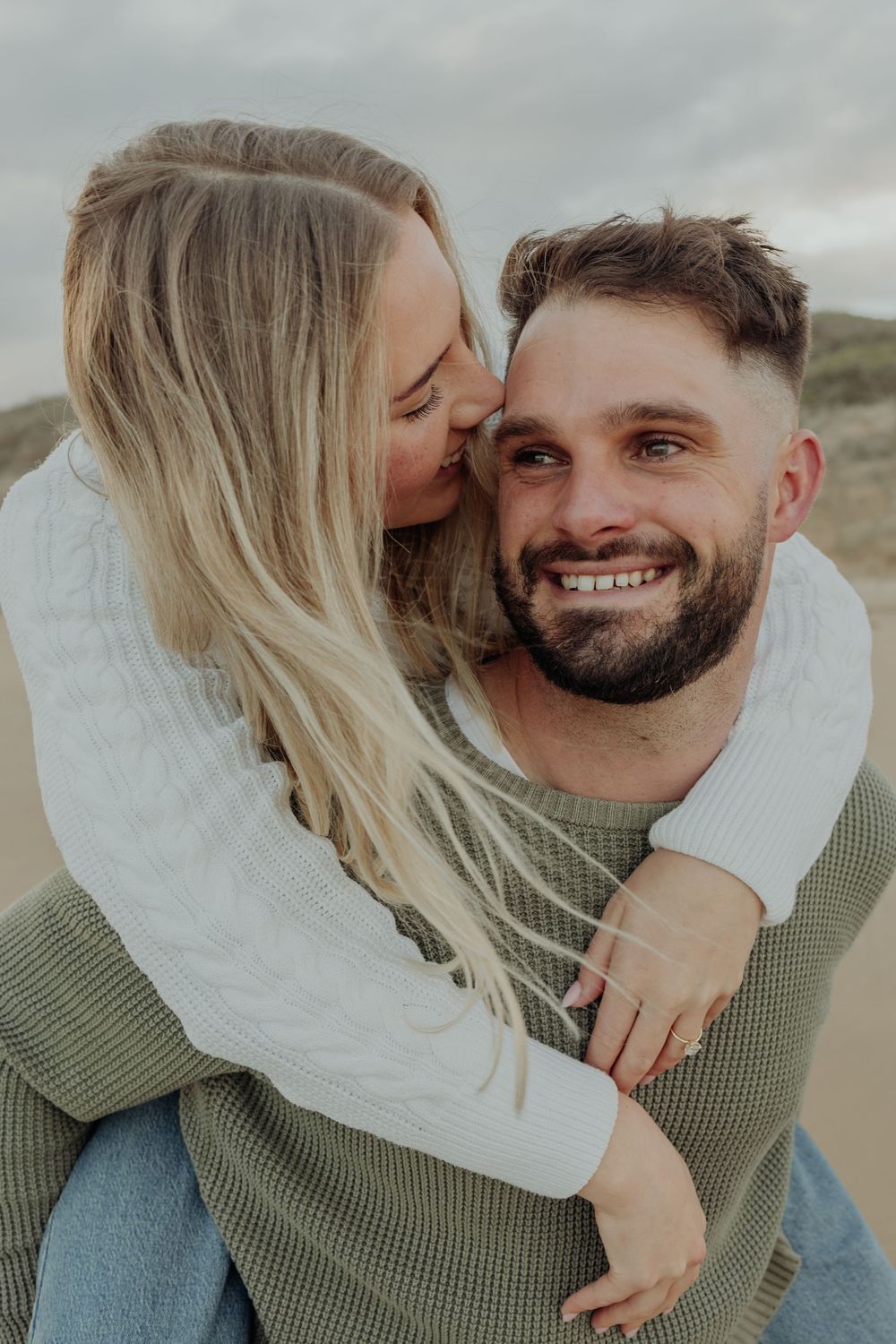 Happy couple sharing a tender moment as woman kisses smiling bearded man giving her a piggyback ride.
