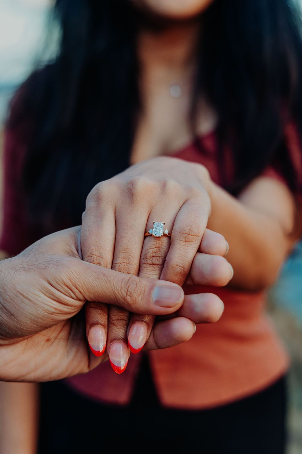 Close-up of a woman's hand displaying a diamond engagement ring while held by her partner.