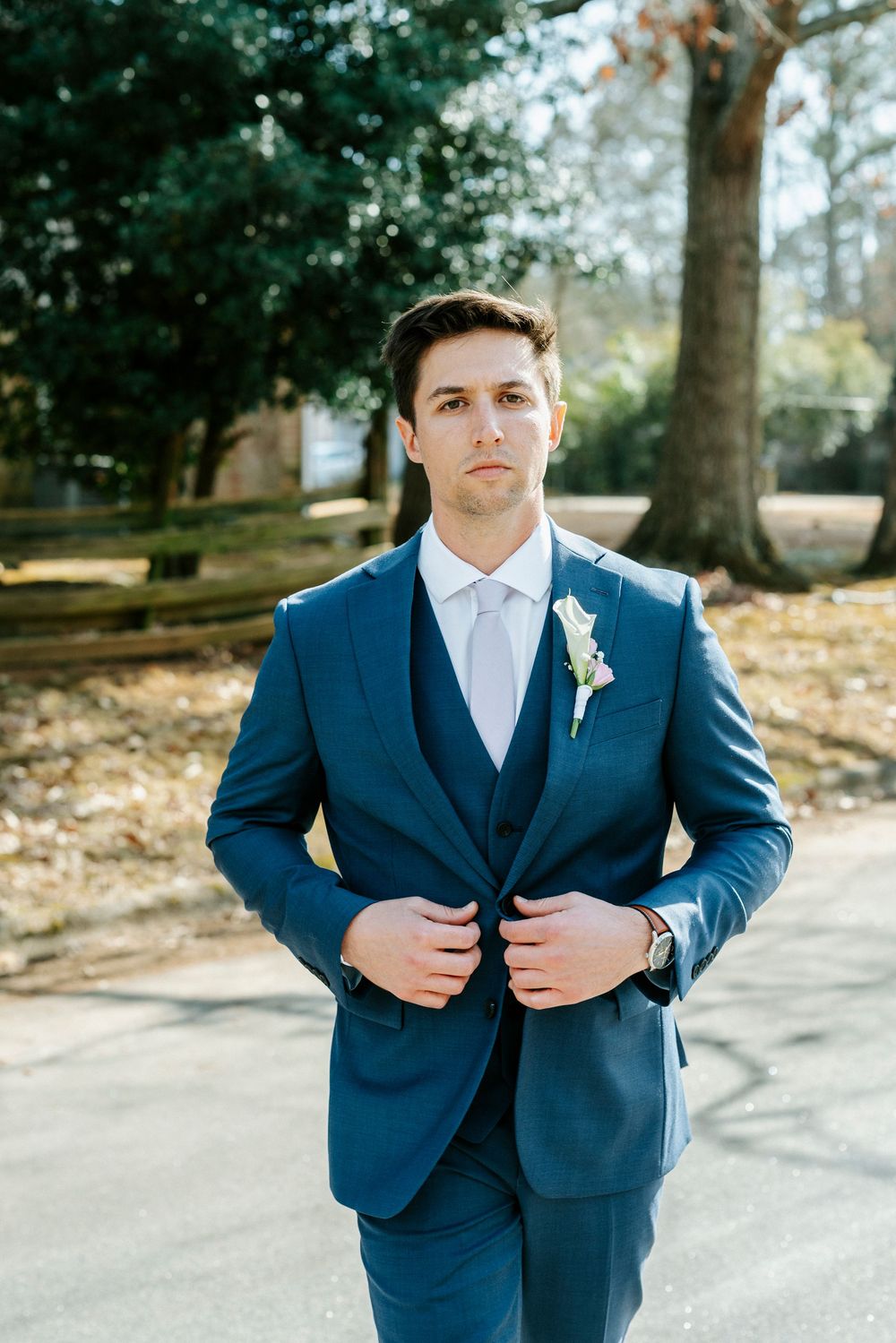 A series of wedding photos showing details of a navy blue suit with boutonniere in an outdoor garden setting.