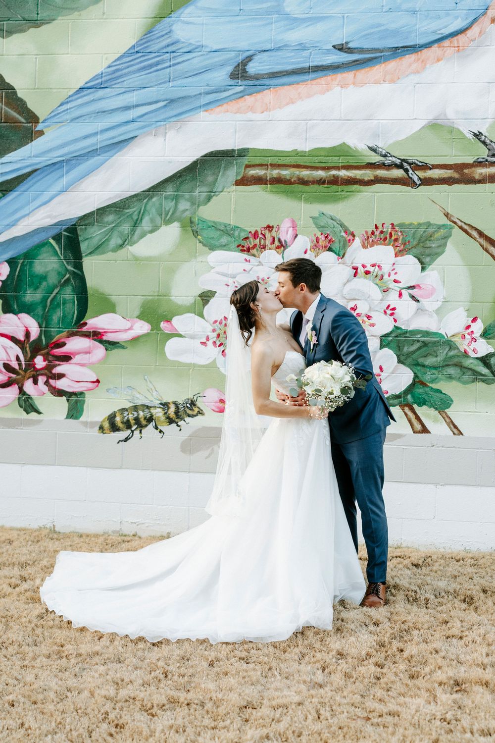 Wedding couple embraces against a whimsical painted wall mural featuring flowers and greenery.