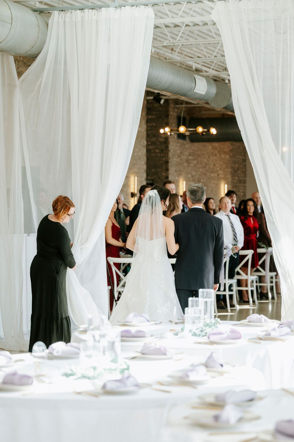 An elegant wedding reception venue with flowing white drapes and table settings in an industrial-style space.