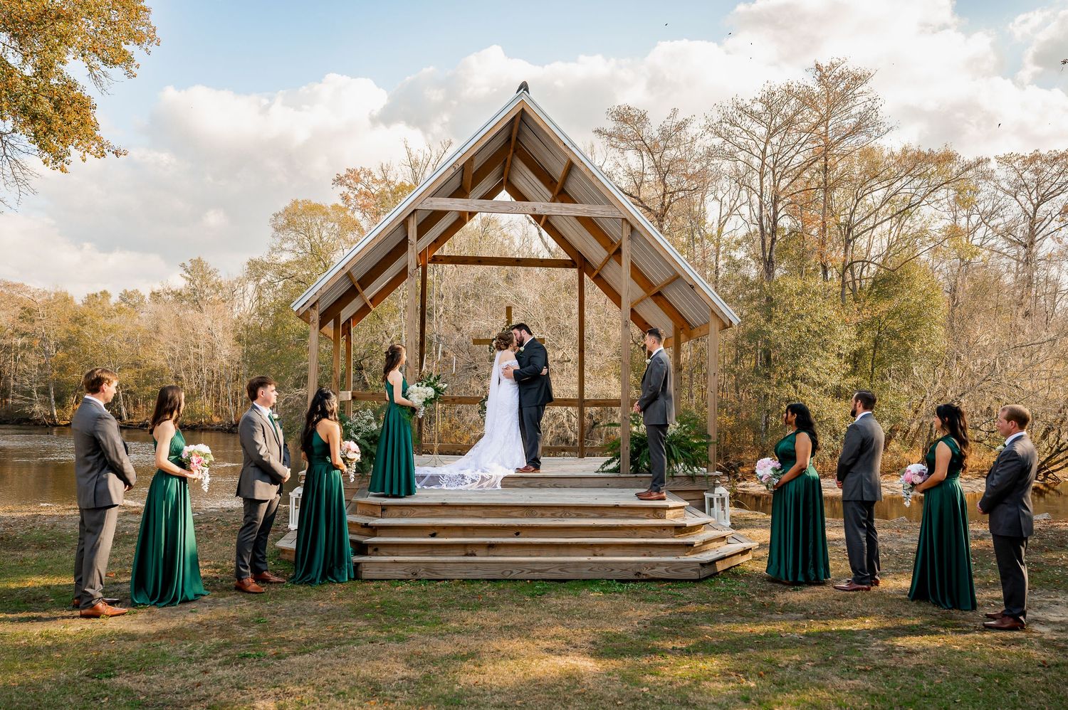 Panoramic view of outdoor wedding ceremony under wooden pavilion surrounded by autumn trees.
