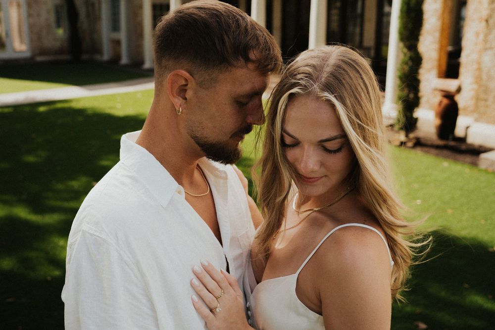 An intimate portrait of a couple in white clothing against a sunlit garden backdrop.