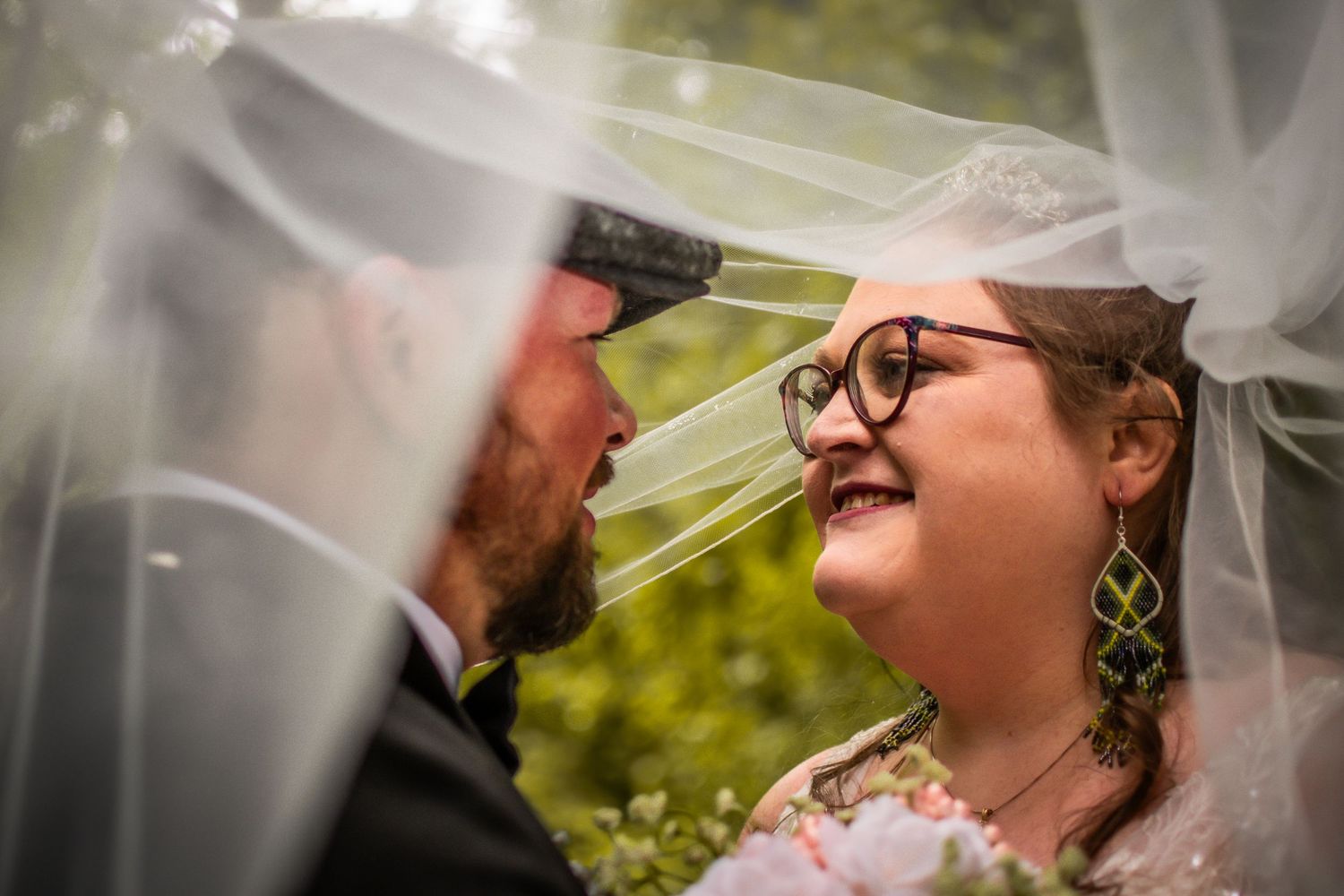 A joyful wedding couple shares a tender moment under a flowing veil in a garden setting.