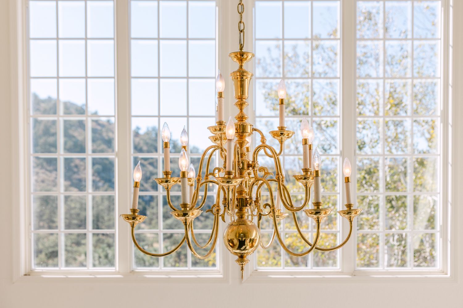 Elegant dining room with gold chandeliers, white walls, and large windows overlooking a scenic mountain landscape.