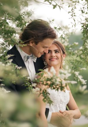 Romantic wedding couple shares an intimate moment among blooming spring tree branches in soft natural light.