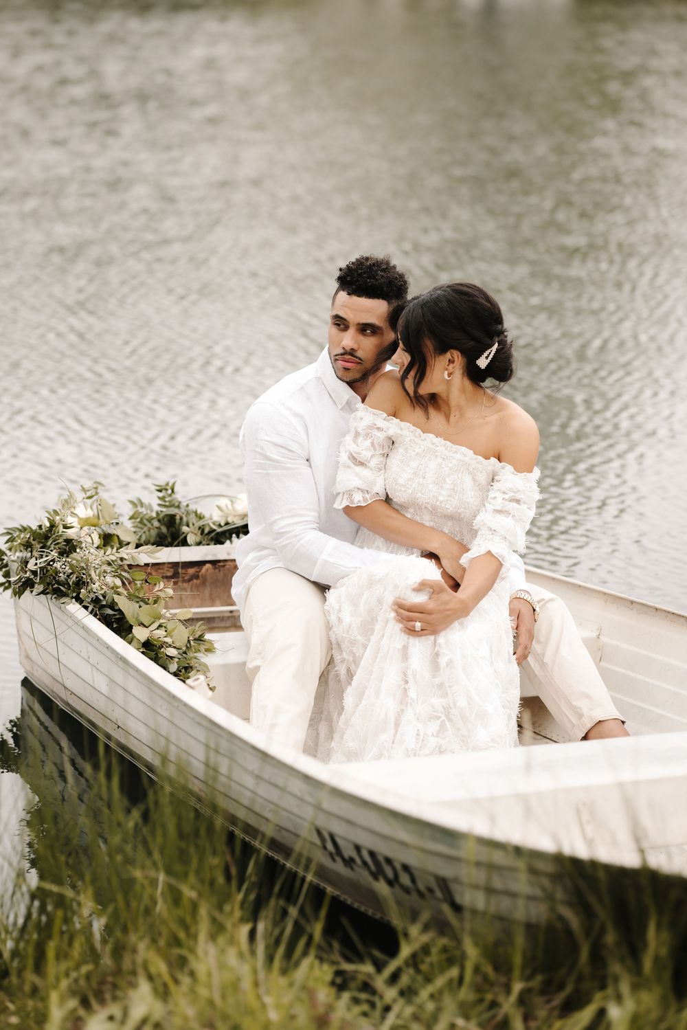 A romantic moment captured in a white rowboat on calm waters with floral decorations.