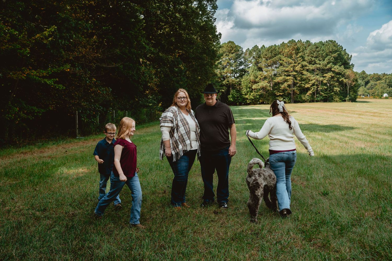 Group of people walking together through a grassy meadow on a sunny day with scattered clouds overhead.