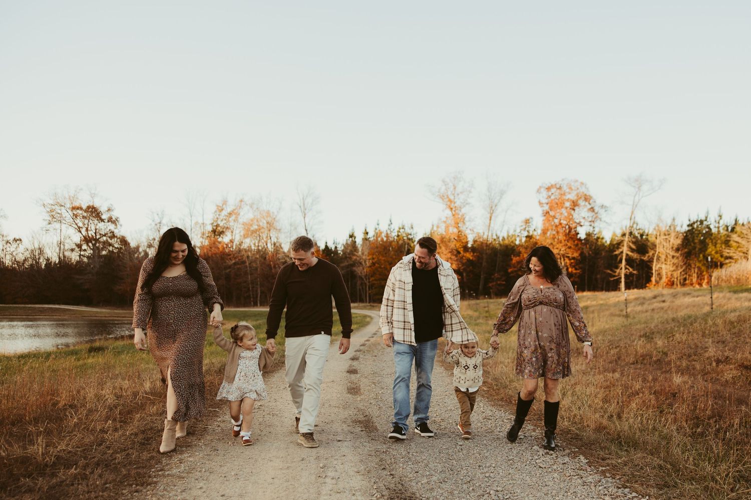 Family of five walking hand-in-hand down a dirt path during golden autumn sunset.
