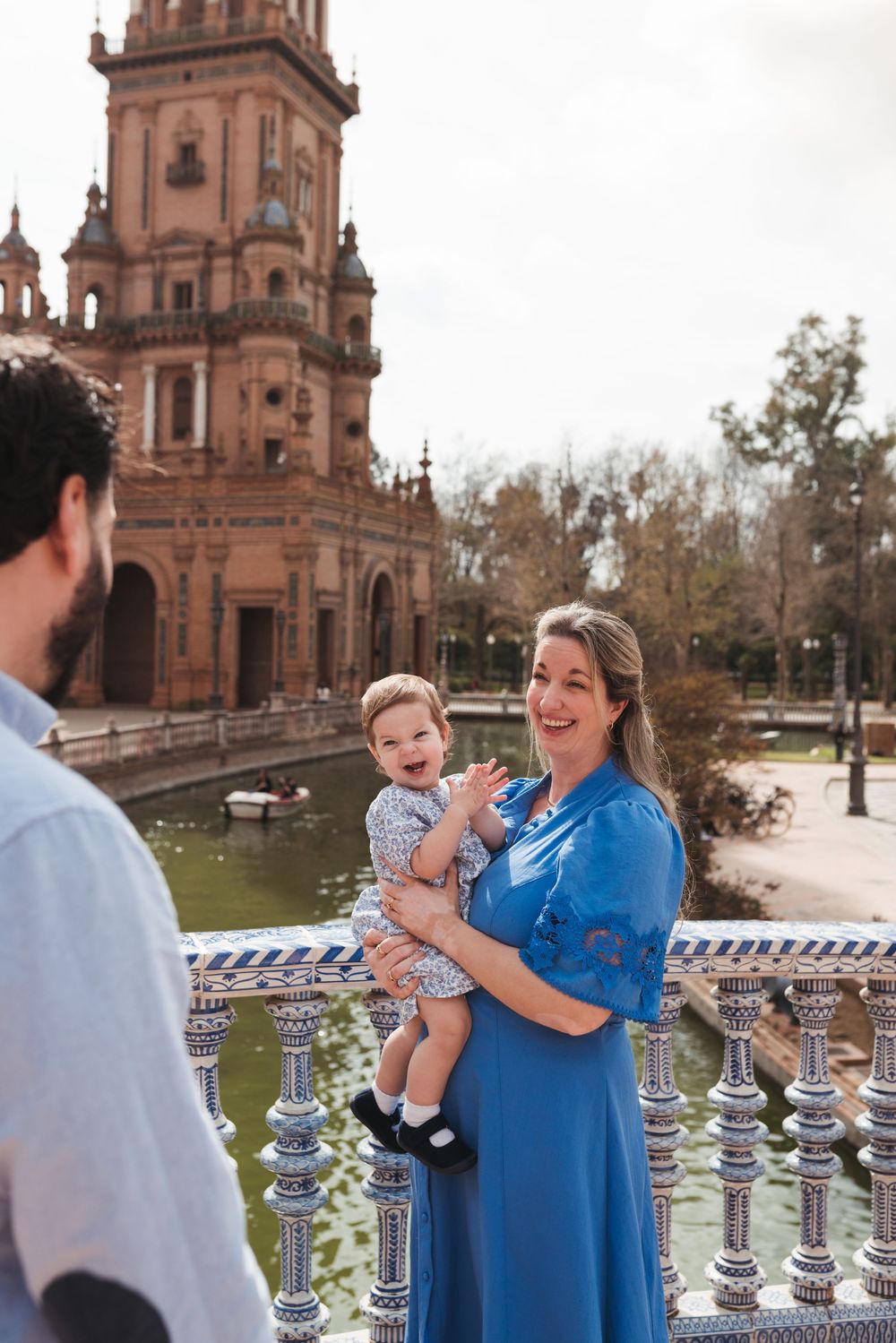 Family enjoying a sunny day together at Plaza de Espana in Seville with ornate architecture and water features in background.