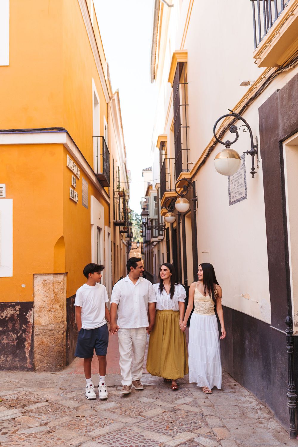 Family of four strolling through a charming narrow cobblestone street in Seville, Spain, lined with colorful buildings.