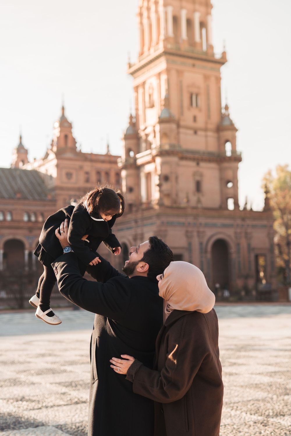 Loving family embracing in front of Plaza de España's ornate architecture during golden hour.