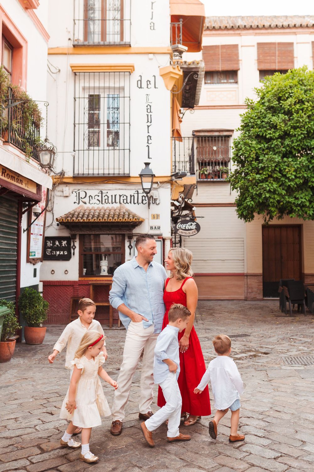 Family of five strolling cobblestone streets in Seville Spain near Restaurant del Laurel on a sunny day.