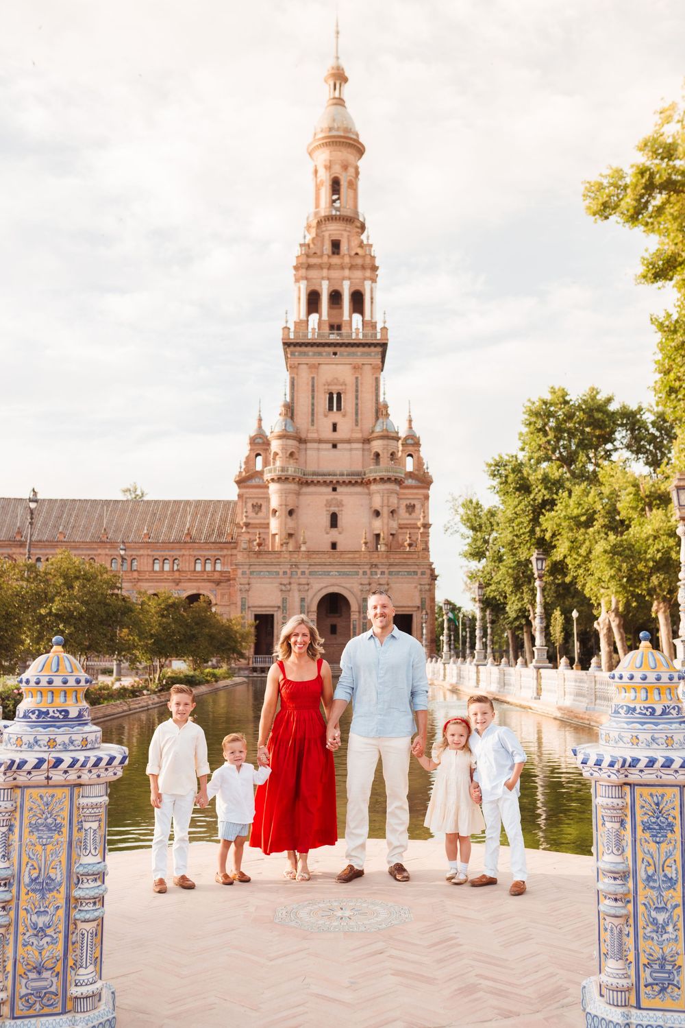 Family posing at Plaza de España in Seville, Spain, with the iconic tower and canal in the background.