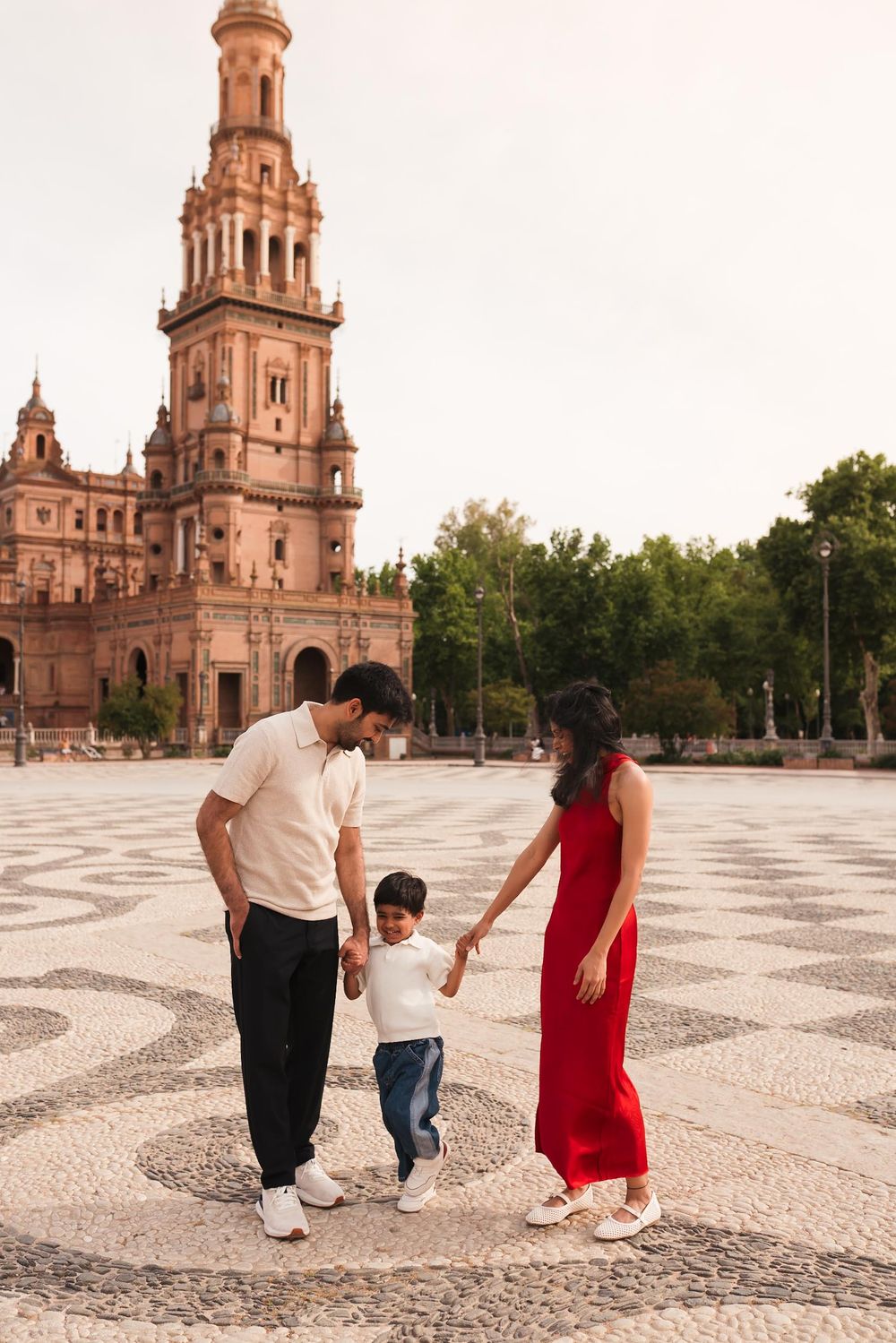Family with toddler holding hands at Plaza de España, Seville, with ornate tower backdrop.
