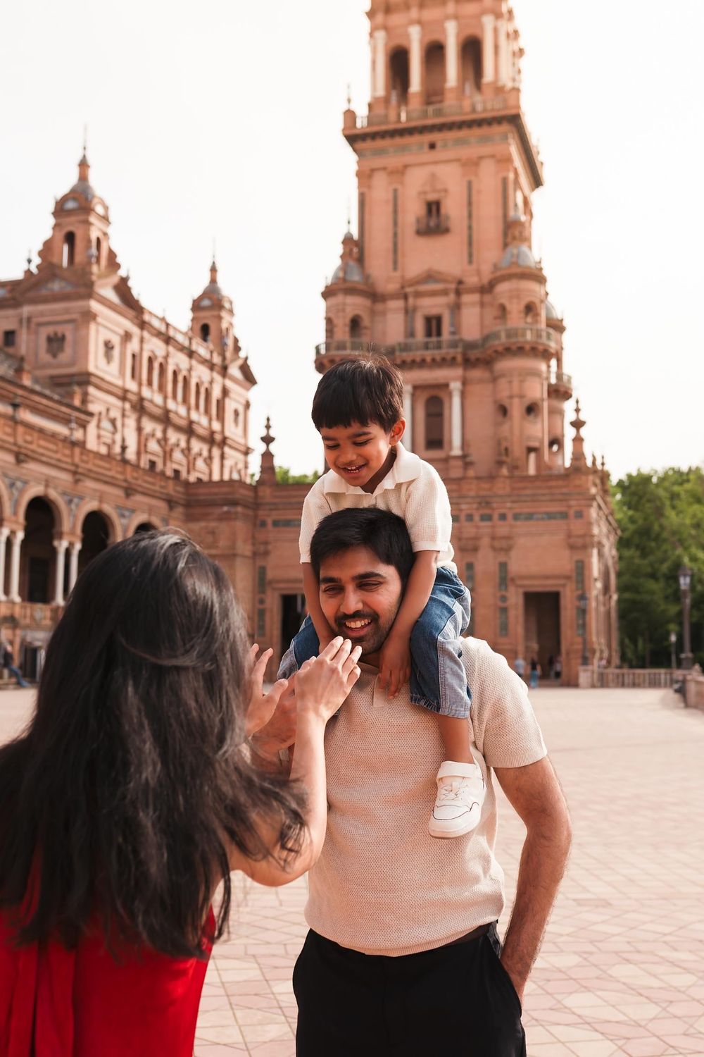 A happy family with a child on dad's shoulders smiling at Plaza de España, Seville, Spain.