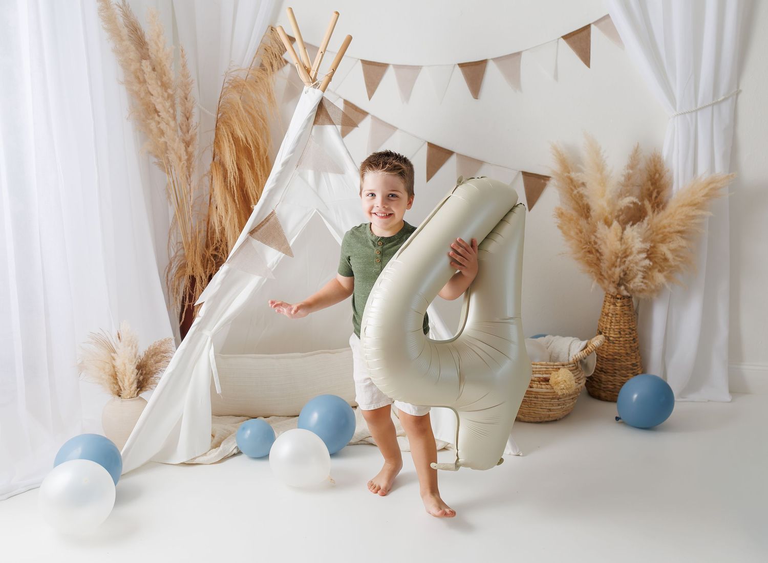 Minimalist white photo studio with blue balloons, bunting, and natural pampas grass decor.