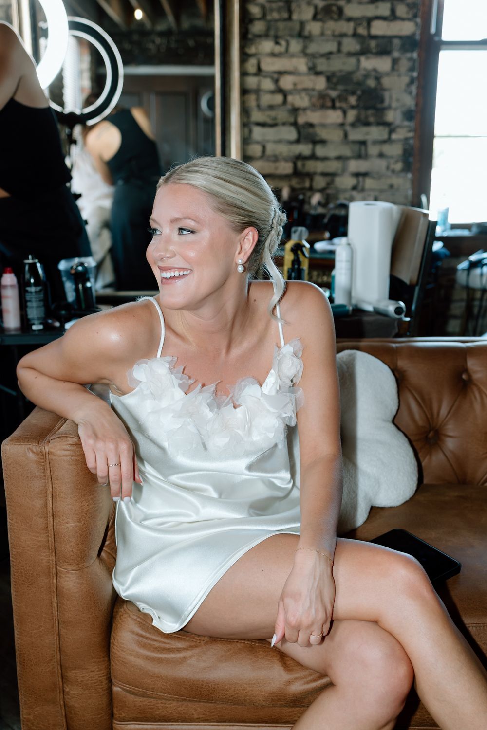 White satin loungewear photographed on a brown leather couch in an industrial-style room.