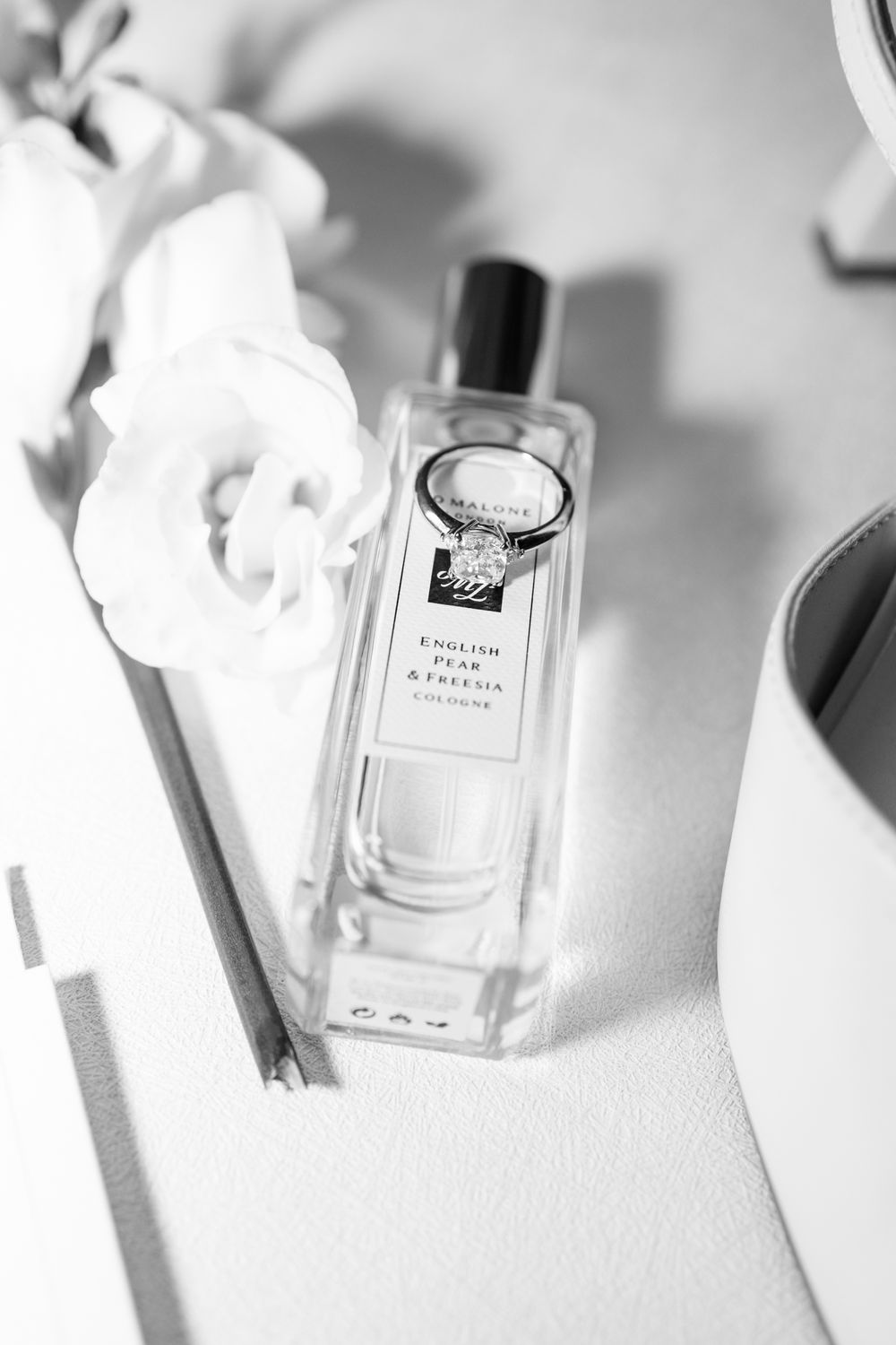 Luxury perfume bottle with white flower on light surface in black and white photography.