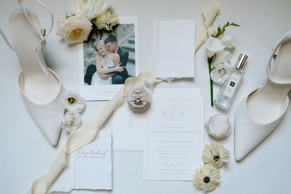 Wedding accessories including white shoes, roses, invitations and ribbons arranged on a light background.