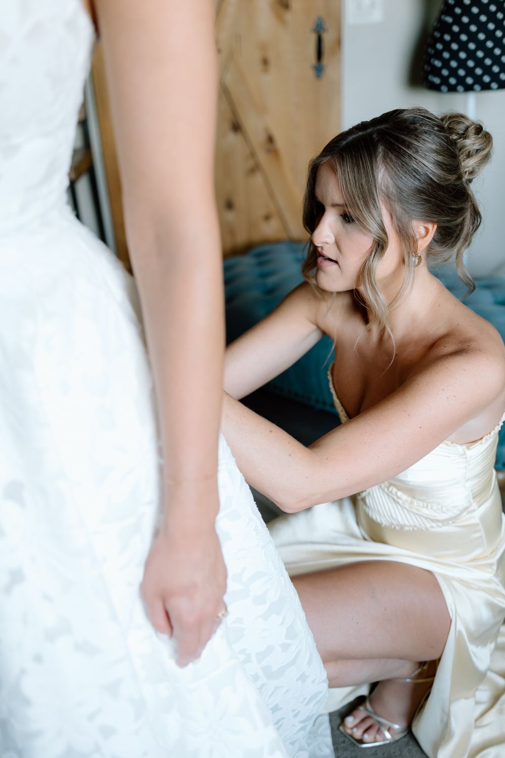 Close-up details of white satin wedding dress being adjusted.