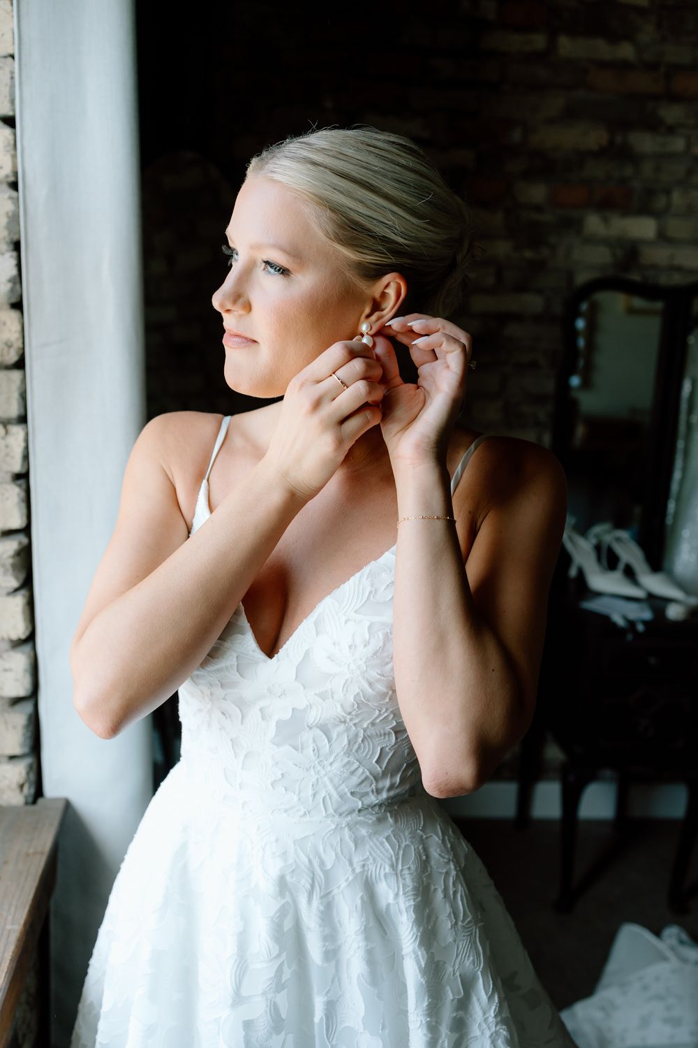 An elegant wedding preparation moment as earrings are put on near a brick wall.