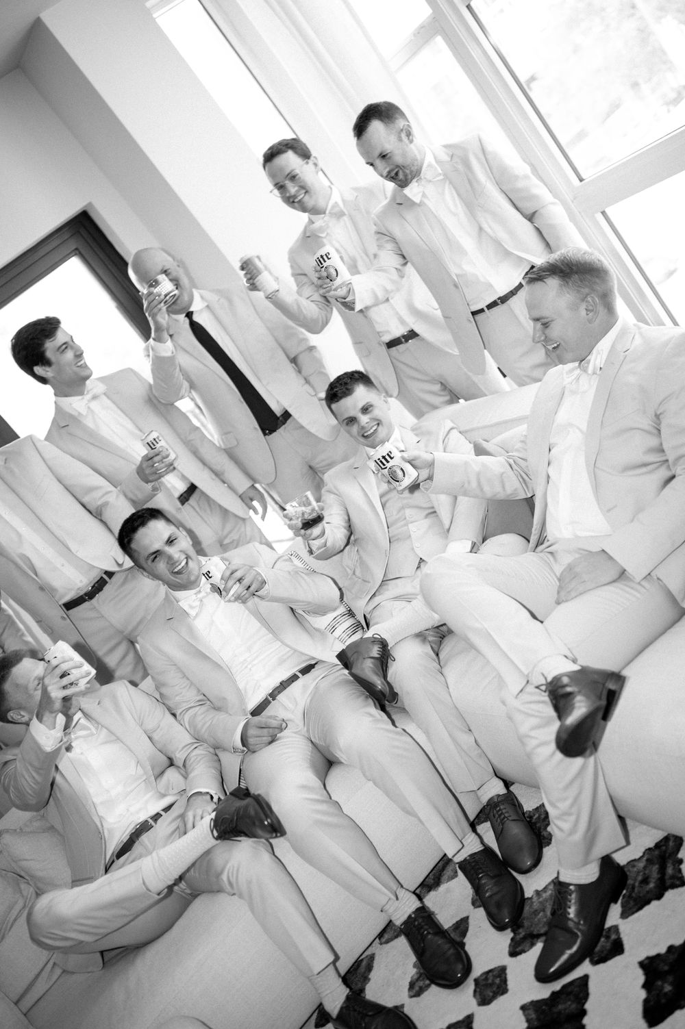 Wedding party members in light colored suits relaxing and socializing indoors.