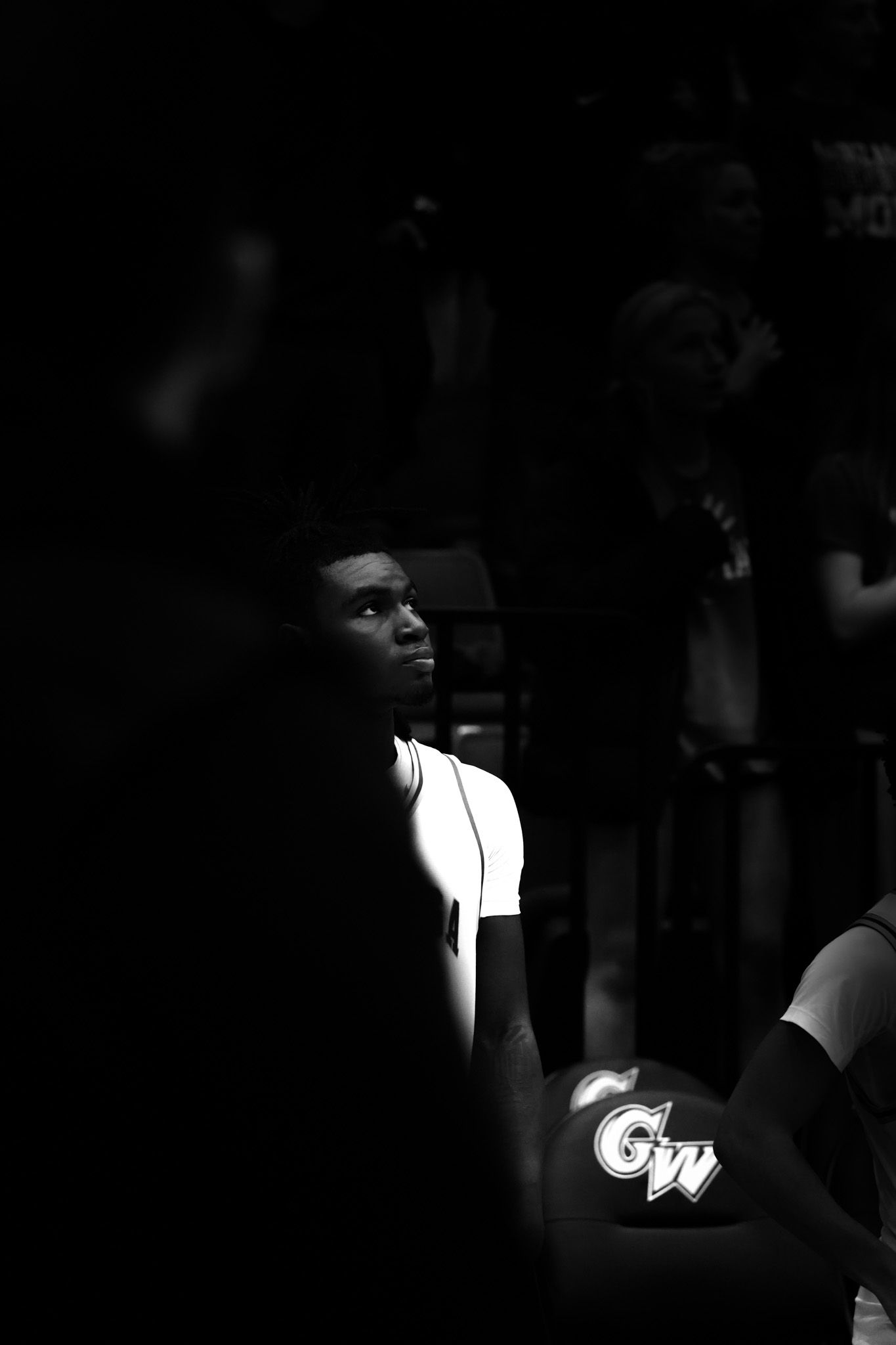 Dramatic black and white photo of a basketball player in white uniform lit against a dark background.