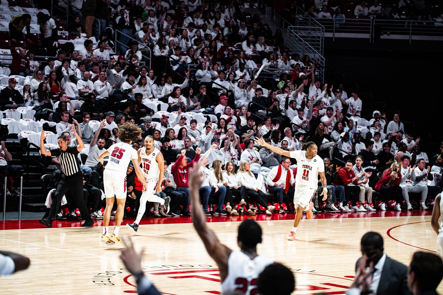 A basketball player takes a shot during a game while a large crowd watches in the arena.