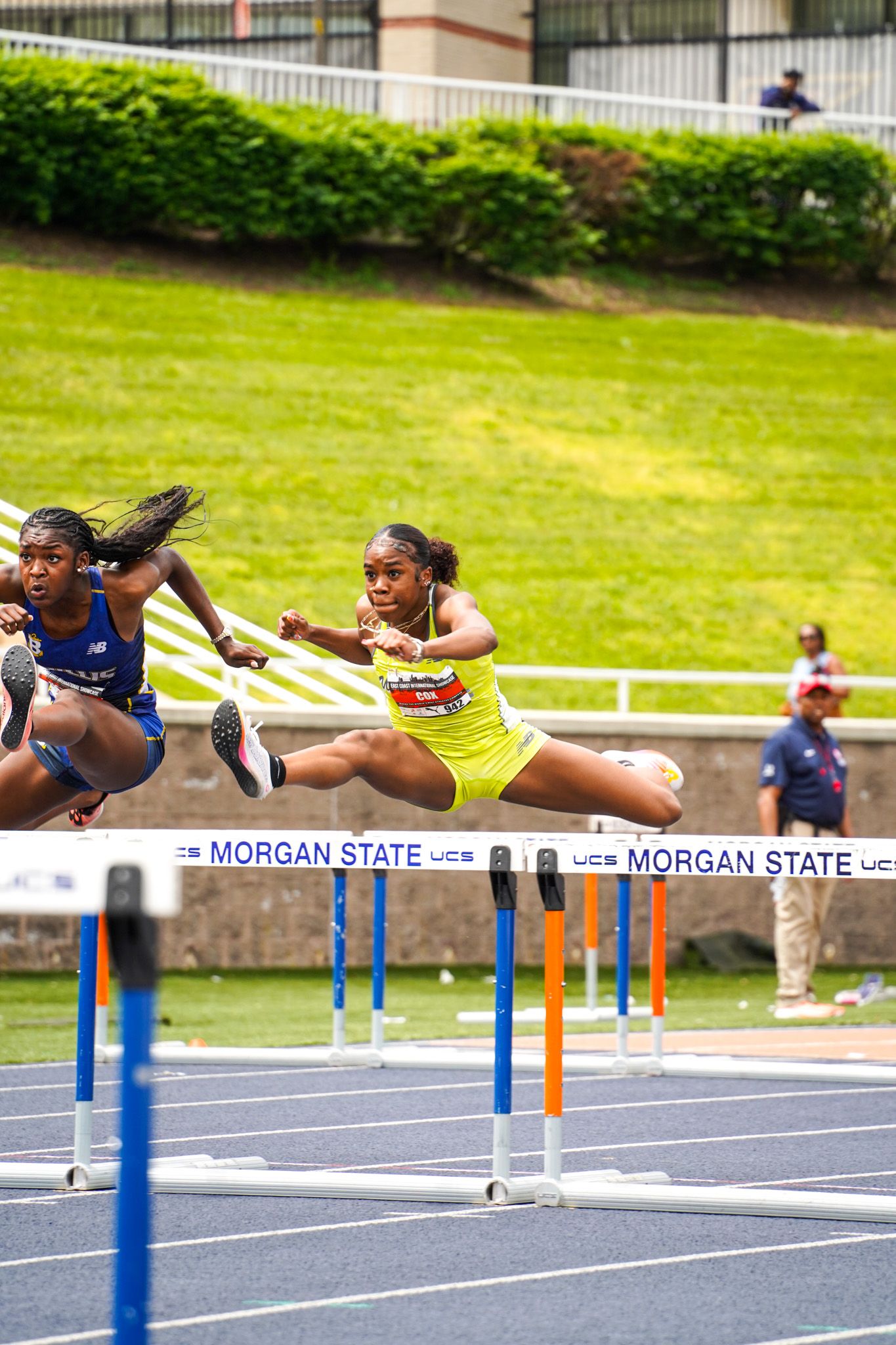 Track and field athletes leap over hurdles during a race at Morgan State University's outdoor track facility.